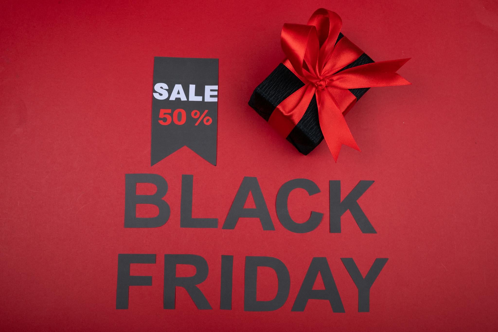 Black Friday sale banner with 50% off tag and gift box wrapped with red ribbon on red background.