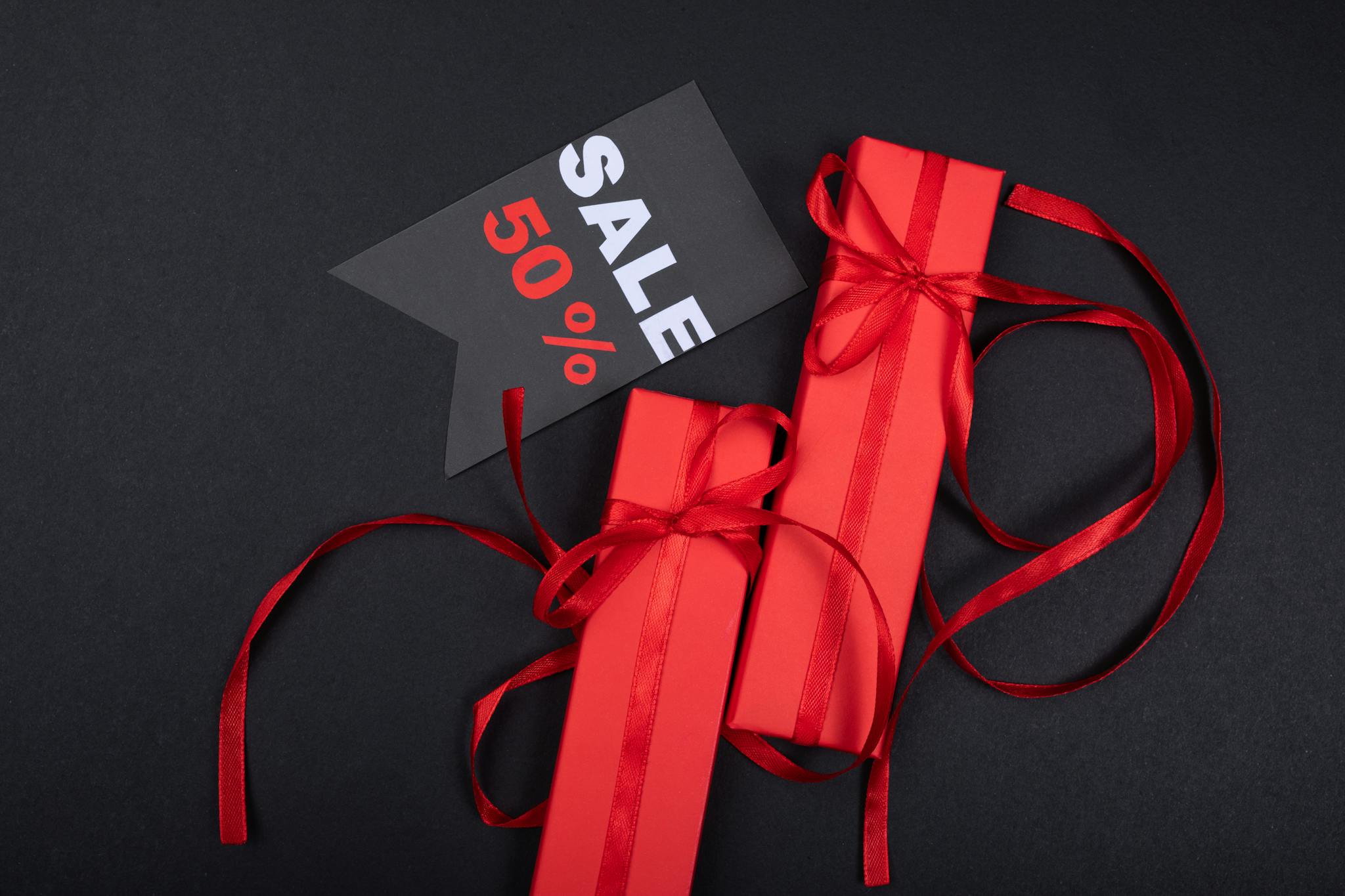 Red gift boxes with ribbons and 50% sale tag against black background.